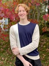 Carter wearing a beige, navy, and white sweater with autumn leaves in the background